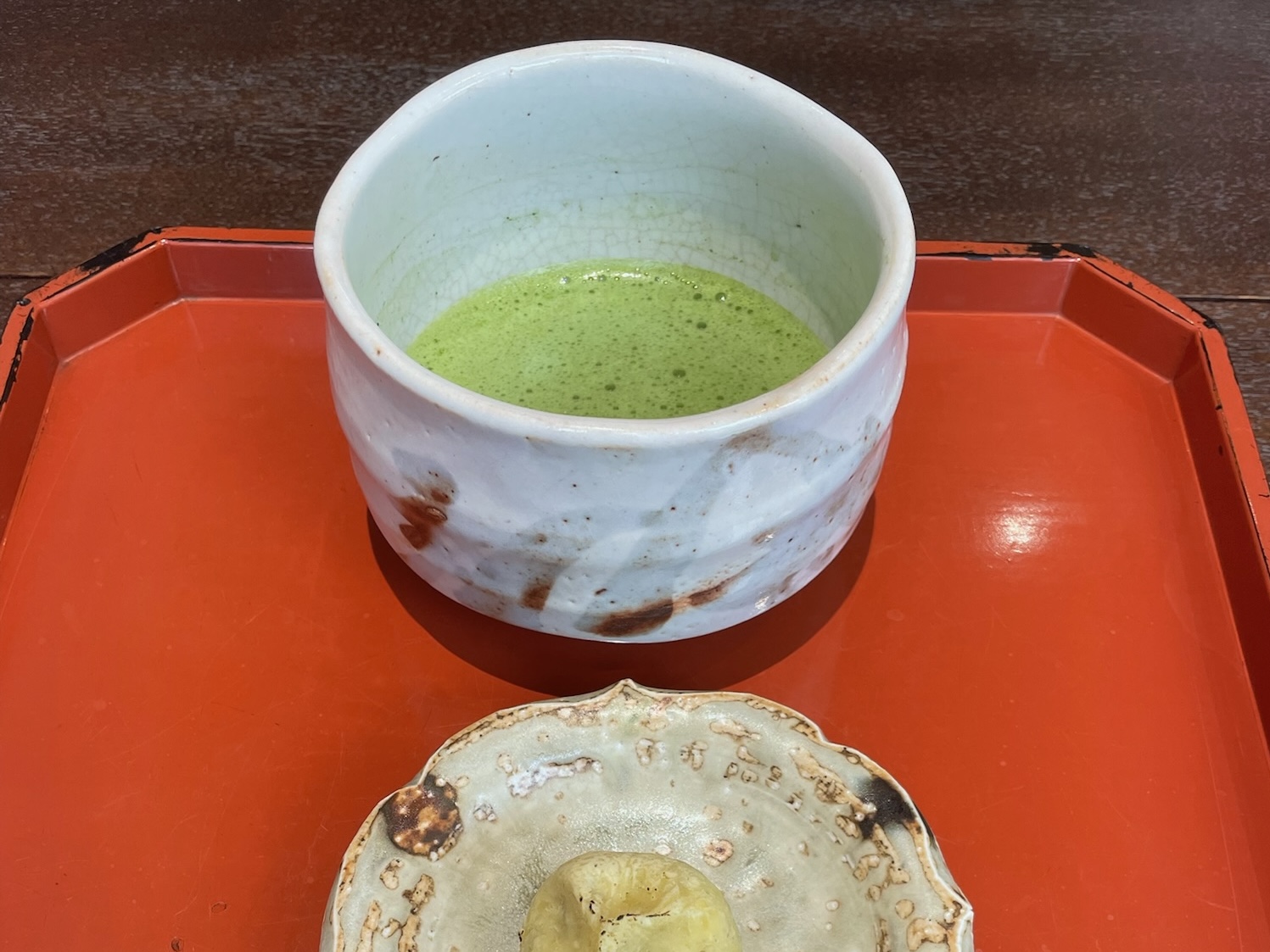 A bowl of matcha and a chestnut-shaped wagashi served on a red tray at Aoyama Beniya